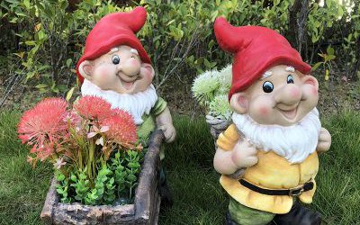 公园草坪上两个玻璃钢彩绘卡通背竹筐和推花盆小推车的小矮人雕塑