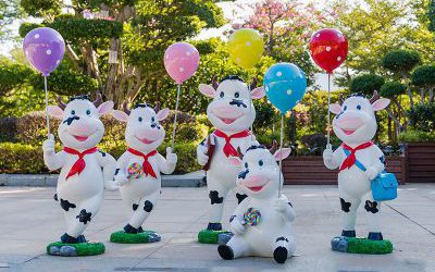 公园一群拿气球的玻璃钢卡通奶牛雕塑