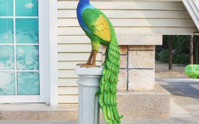 花园里一只立在石柱上的玻璃钢彩绘孔雀雕塑